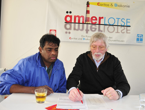 Älterer Mann hilft jüngerem beim Ausfüllen eines Formulars